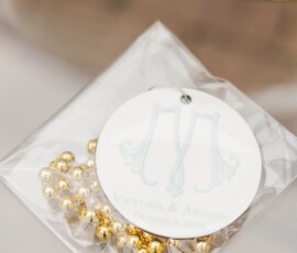 Gold and silver beaded bag with M tag and wedding details, on reflective surface — unique ceremony décor idea.