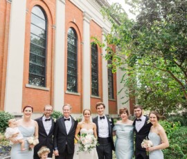 Wedding party in formal attire outside Louisiana brick building, bridesmaids in light blue, groomsmen in black tuxedos.