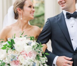 Bride in strapless gown and veil smiles at groom in tux as they walk outdoors after their Louisiana wedding ceremony.