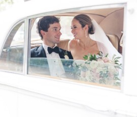 Bride and groom smiling in the back of a classic white car after their New Orleans wedding, holding flowers and enjoying the moment.