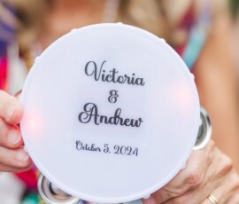 White tambourine reading “Victoria & Andrew, October 5, 2024” held at a vibrant New Orleans wedding celebration.