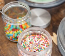 Jars of rainbow sprinkles and mini M&M candies on a wooden table with ice cream tubs—fun Louisiana wedding dessert inspo.