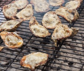 Grilled oysters with seasoned topping cook over hot coals, smoke rising—ideal for Louisiana or Gulf South wedding inspiration.