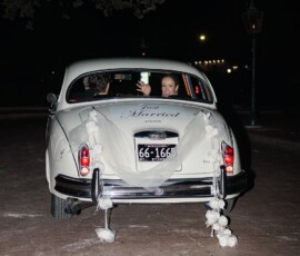 Bride and groom wave from a classic white car with Just Married sign and tin cans after their New Orleans wedding at night.