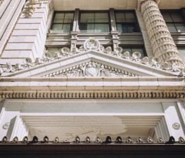 The Ritz-Carlton New Orleans entrance with ornate details and triangular pediment, seen from below on a sunny day.
