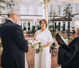 Bride in a white jumpsuit smiles at groom during outdoor Louisiana wedding with officiant—Gulf South wedding inspiration.