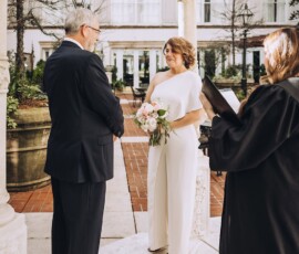Couple under a gazebo at a Gulf South wedding; bride in white with bouquet, groom in dark suit, officiant reading nearby.