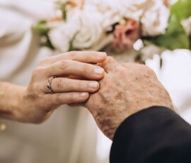 Placing a ring on a finger at an elegant Louisiana wedding, with flowers in the background.