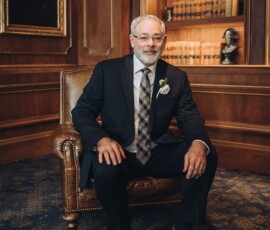 Older man in a suit sits on a leather chair in an elegant wood-paneled library, evoking refined New Orleans wedding inspiration.
