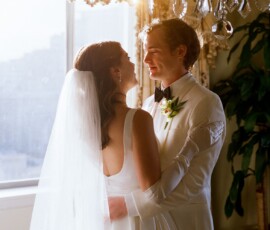 Bride and groom smile and embrace by a sunlit window at their elegant New Orleans wedding.