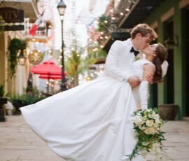Bride in white gown and groom in white tuxedo dip on a city street, surrounded by lights at a Louisiana wedding.