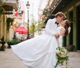 Bride and groom kiss as he dips her on a decorated New Orleans street with string lights during their wedding.