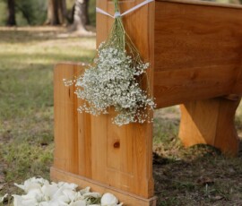 Wooden bench with baby’s breath bouquet and ribbon, white rose petals on grass, outdoors among trees at a Louisiana wedding.