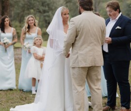 Bride and groom at outdoor Louisiana wedding, with bridesmaids in blue, flower girl in white, and officiant holding a book.