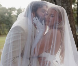 Bride and groom embrace under a sheer veil outdoors, smiling amid trees after a New Orleans wedding ceremony.