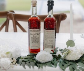 Two whiskey bottles on a white table with flowers, greenery, and a taper candle, set for an elegant New Orleans wedding.