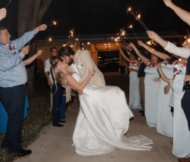 Bride and groom kiss as he dips her under sparklers held by loved ones at their Louisiana wedding celebration.