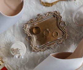 White bridal shoes, gold tray with rings, perfume, pearl earrings, and shell on lace—New Orleans wedding inspiration.
