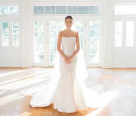 Bride in strapless white gown smiles in bright room with wooden floors and large windows before the ceremony.