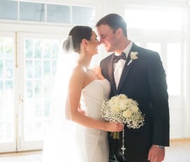 Bride in white dress with bouquet smiles beside groom in tuxedo, celebrating their joyful New Orleans wedding indoors.