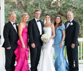 Bride, groom, and four adults smile together on a porch amid greenery at their joyful New Orleans wedding.