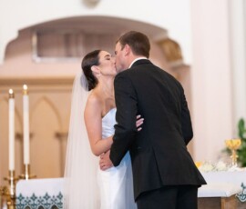 Bride and groom kiss at their Louisiana wedding in front of an altar with candles and chalices.