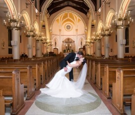 Bride and groom kiss as he dips her in a grand, chandelier-lit church aisle, capturing timeless New Orleans wedding style.