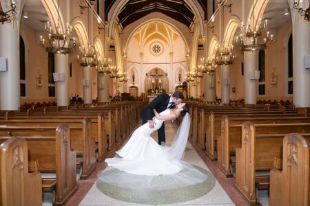 Bride and groom kiss as he dips her in a grand, chandelier-lit church aisle, capturing timeless New Orleans wedding style.