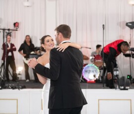 Bride and groom dance as a live band sets up on stage in a bright, elegant Louisiana wedding venue.