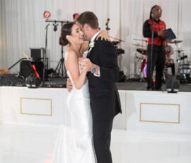 Bride and groom joyfully dance and embrace on a white floor at their Gulf South wedding as a live band plays.