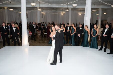 Bride and groom share their first dance on a white floor, surrounded by wedding party and guests in a decorated Louisiana ballroom.