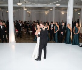 Bride and groom share their first dance on a white floor, surrounded by wedding party and guests in a decorated Louisiana ballroom.