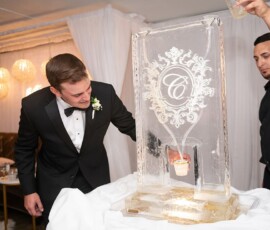 Man in tuxedo gets a drink poured from an ice sculpture at an elegant New Orleans wedding with glowing decor.