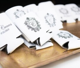 White drink koozies with a C monogram and “The Cuevas 11.02.2024” on a gold tray, ideal for New Orleans weddings.