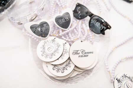 Heart and round sunglasses with “The Cunnes 11.02.24” on the lenses, tags, and beaded necklaces as Louisiana wedding favors.