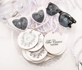 Heart and round sunglasses with “The Cunnes 11.02.24” on the lenses, tags, and beaded necklaces as Louisiana wedding favors.