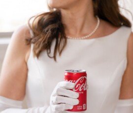 Woman in white dress, pearl necklace, and gloves holds Coca-Cola can—chic Louisiana wedding inspiration.