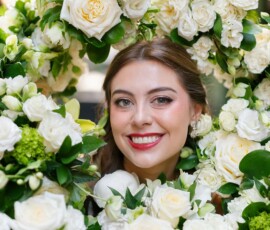 Smiling woman with brown hair surrounded by white roses and green leaves at an elegant Louisiana wedding.