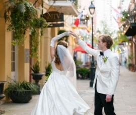 Bride and groom twirl on a plant-lined New Orleans street with string lights, celebrating their wedding.