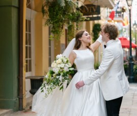 Smiling bride and groom embrace on a city sidewalk, with greenery and buildings in the background at a Louisiana wedding.