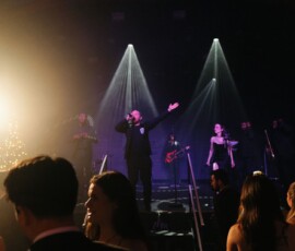 Band performing on stage with spotlights and a Christmas tree as guests in formal wear dance at a New Orleans wedding.