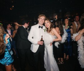 Couple in white tuxedo and dress pose at a lively Louisiana wedding, surrounded by dancing guests.