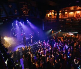 Live music on a purple-lit stage entertains a lively crowd in a stylish, art-filled two-level Gulf South wedding venue.