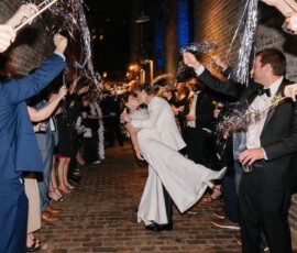 Bride and groom kiss in a cobblestone alley as guests cheer and wave sparklers at their Louisiana wedding.
