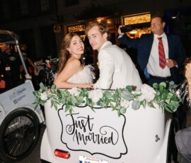 Newlyweds smile in a flower-filled car with a Just Married sign at night, capturing New Orleans wedding joy.