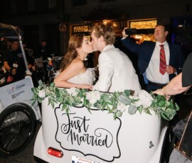 Newlyweds kiss in a white pedicab with a Just Married sign as guests celebrate at their New Orleans wedding.