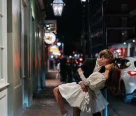 Formally dressed couple shares a romantic dip and kiss at night under Broussards’ sign, inspiring New Orleans weddings.
