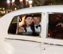 Bride in white dress and groom in tuxedo smile in back of classic white car at night—New Orleans wedding inspiration.