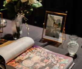 Open book with colorful illustration beside white flowers, photo frame, and glass pitcher on dark tablecloth at Gulf South wedding.