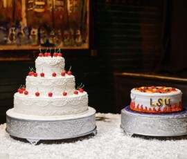 Two ornate cakes: a white, cherry-topped wedding cake and a single-tier LSU cake with orange and yellow icing flames.